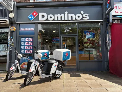 Two Otto mopeds with Domino’s boxes outside a Domino’s store